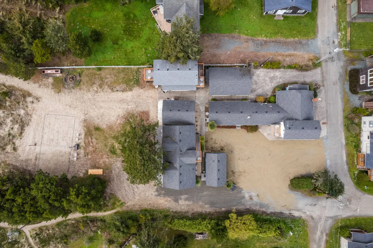 A cluster of buildings is surrounded by an open sandy area and lush greenery. The space feels communal and relaxed, ideal for outdoor gatherings or letting pets enjoy the outdoors with their owners.