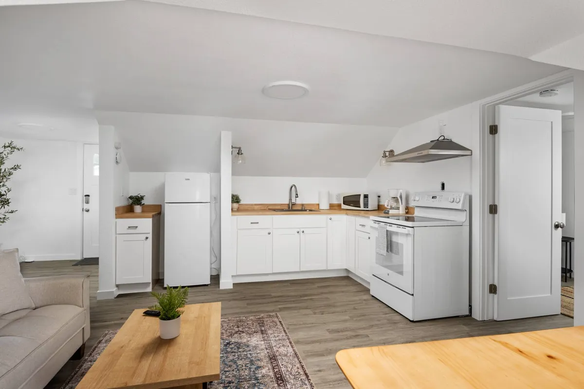 A cozy, well-lit interior view featuring kitchen appliances, a dining table, and a comfortable sofa in the background. The scene communicates warmth, functionality, and the ability to enjoy meals or relax indoors.