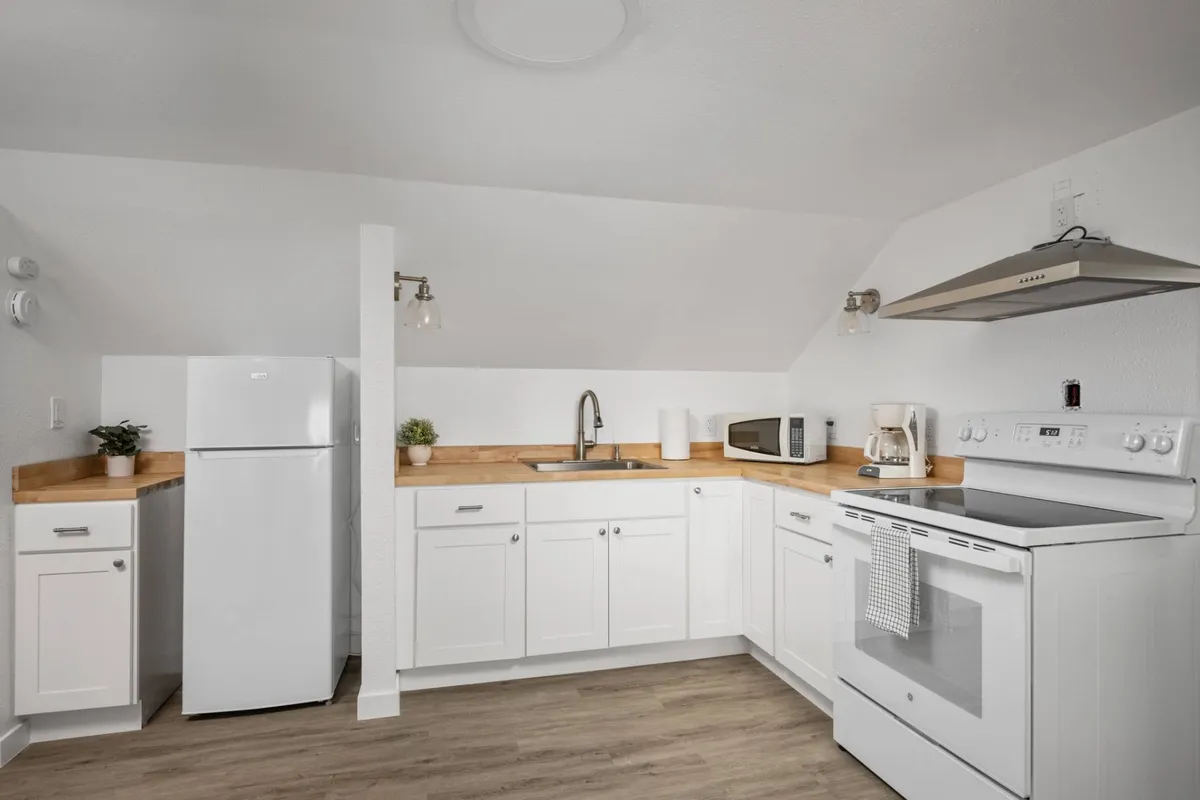 This image features a modern kitchen with crisp white cabinetry, a wood countertop, and stainless steel appliances that create a fresh and inviting atmosphere. The space is well-lit, signifying natural light, and the setup is ideal for home cooking, family gatherings, or quiet mornings with a cup of coffee.